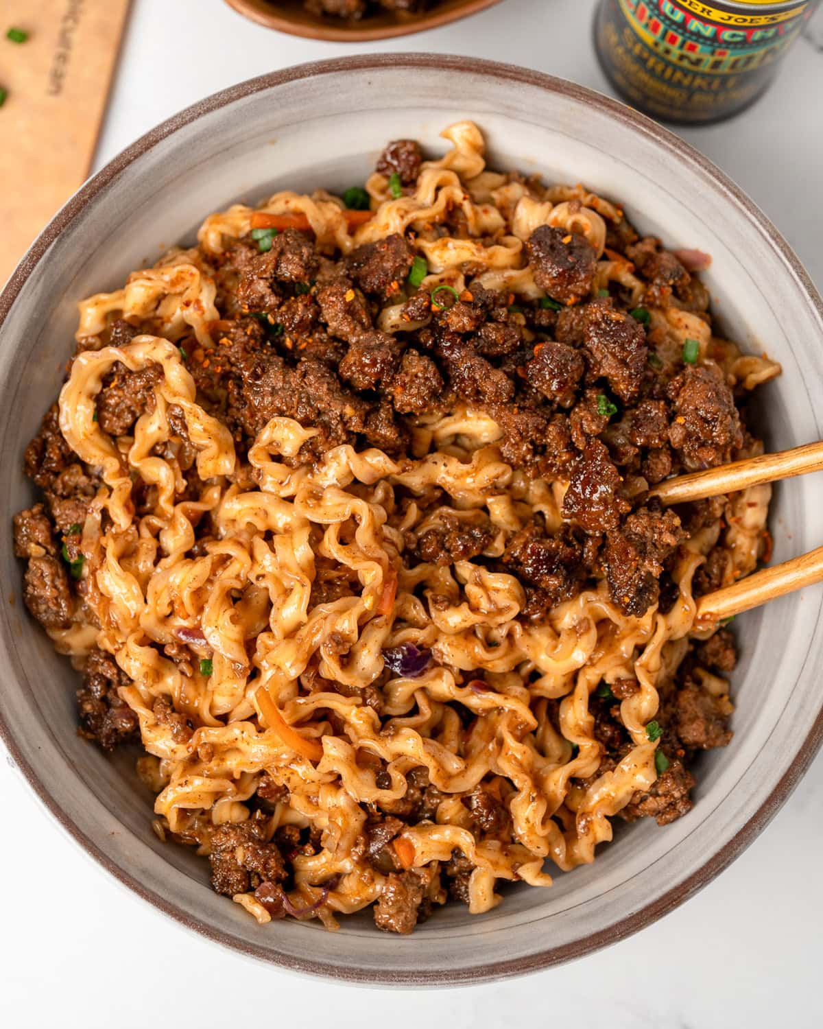 chopsticks in a bowl of noodles with crispy ground beef, sautéed coleslaw mix, and a hoisin sauce