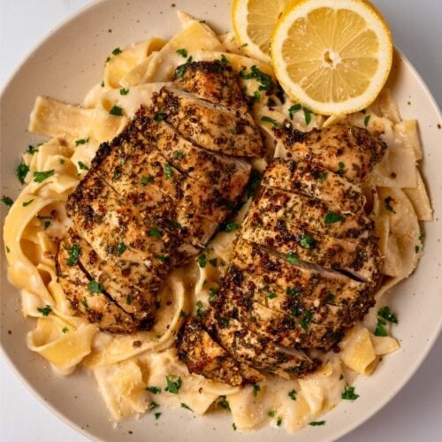 two air fried chicken breasts in a bowl with pasta alfredo and lemon slices