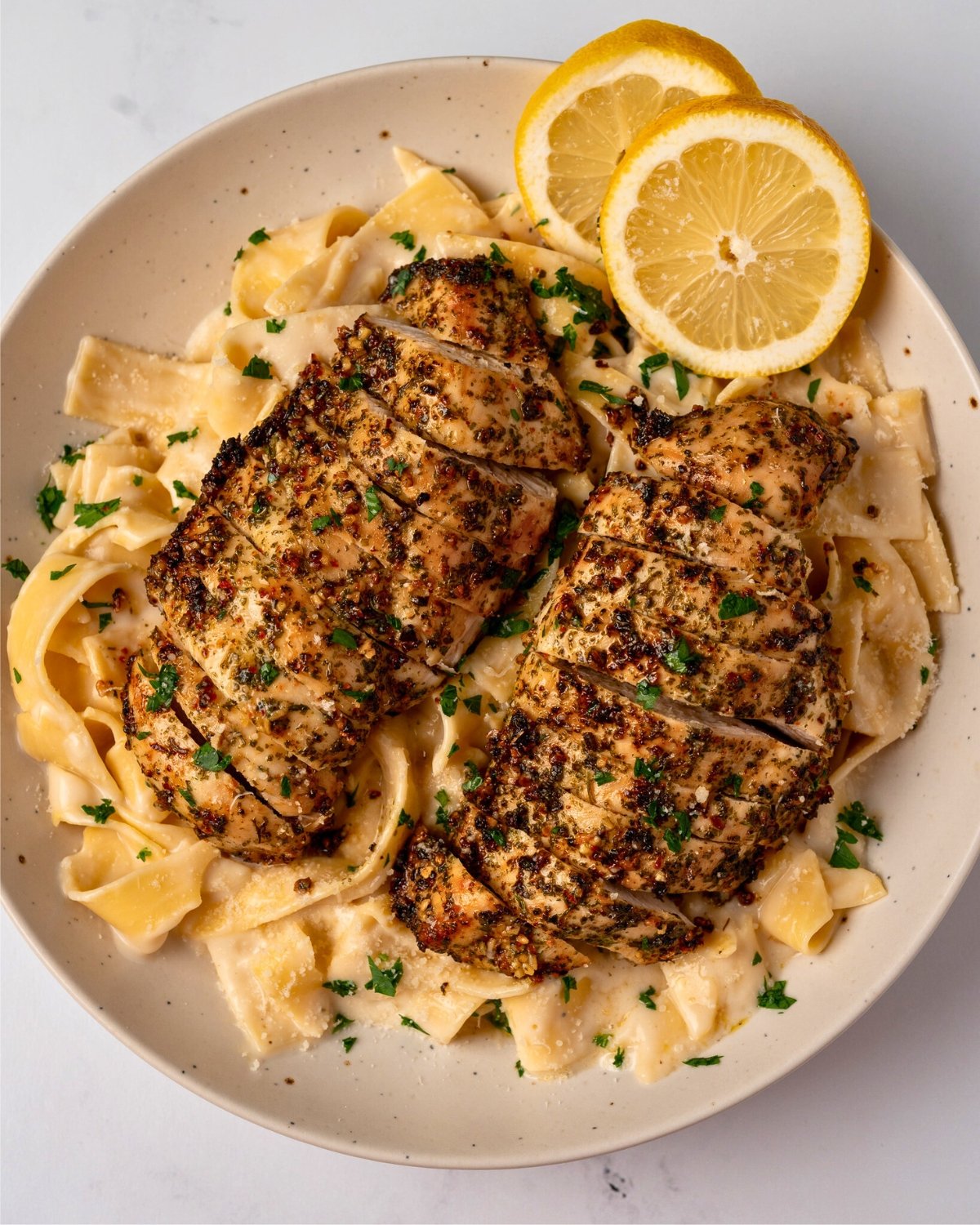 two air fried chicken breasts in a bowl with pasta alfredo and lemon slices