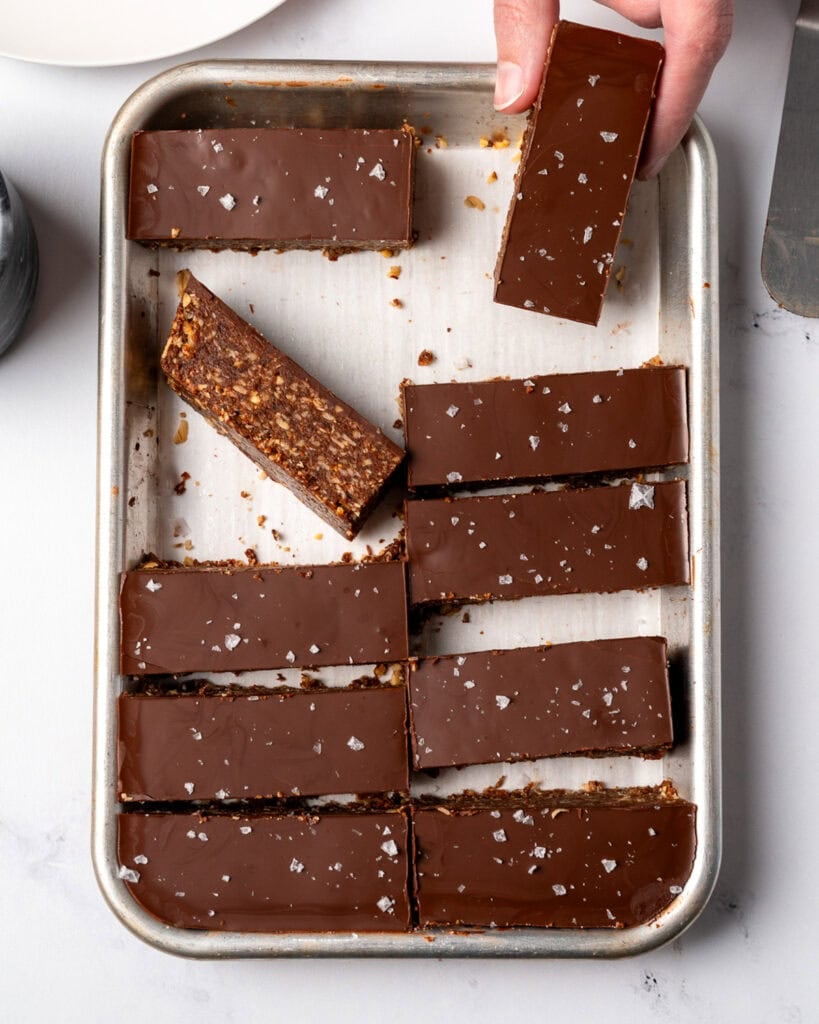 picking up a chocolate granola bar from a sheet pan with sliced bars on it