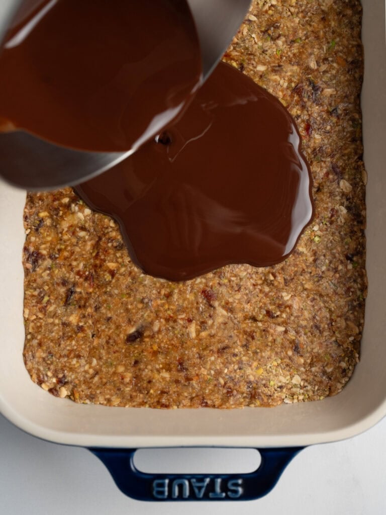 pouring melted chocolate and olive oil over a dish of formed granola bars