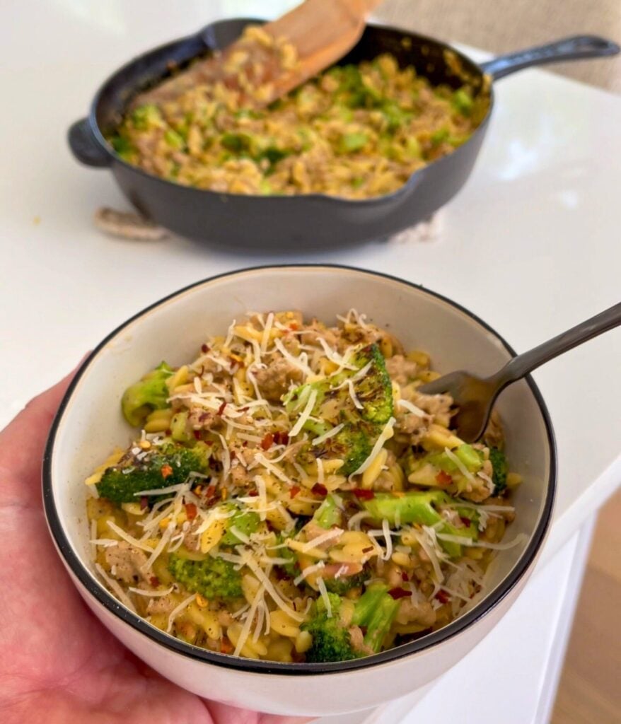 holding a bowl of turkey and broccoli orzo with grated parmesan garnish