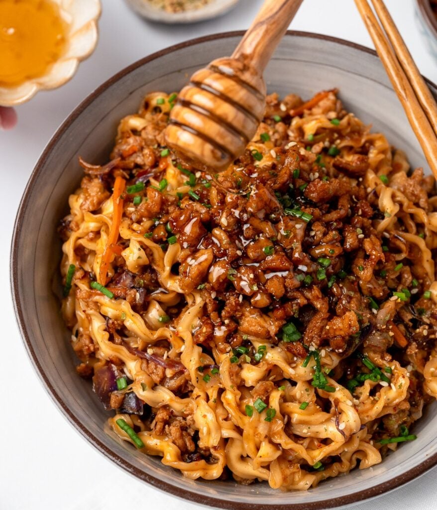 drizzling honey over a noodle bowl with garlic ground chicken crumbles