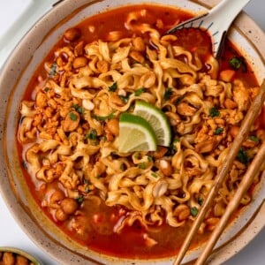 Thai red curry ground turkey and broth in a bowl with Trader Joe's squiggly knife cut noodles, cilantro, and lime wedges