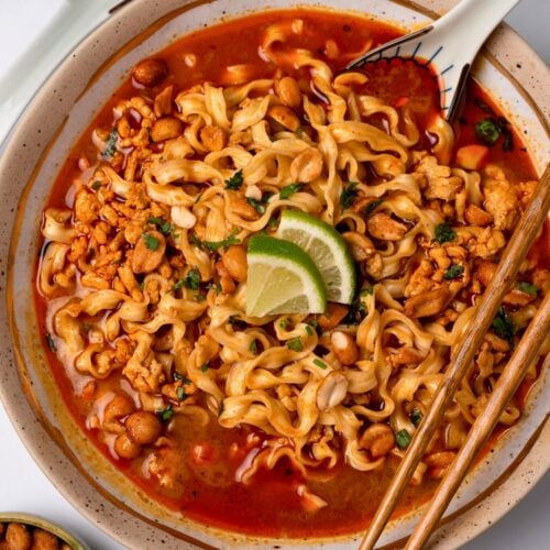 Thai red curry ground turkey and broth in a bowl with Trader Joe's squiggly knife cut noodles, cilantro, and lime wedges