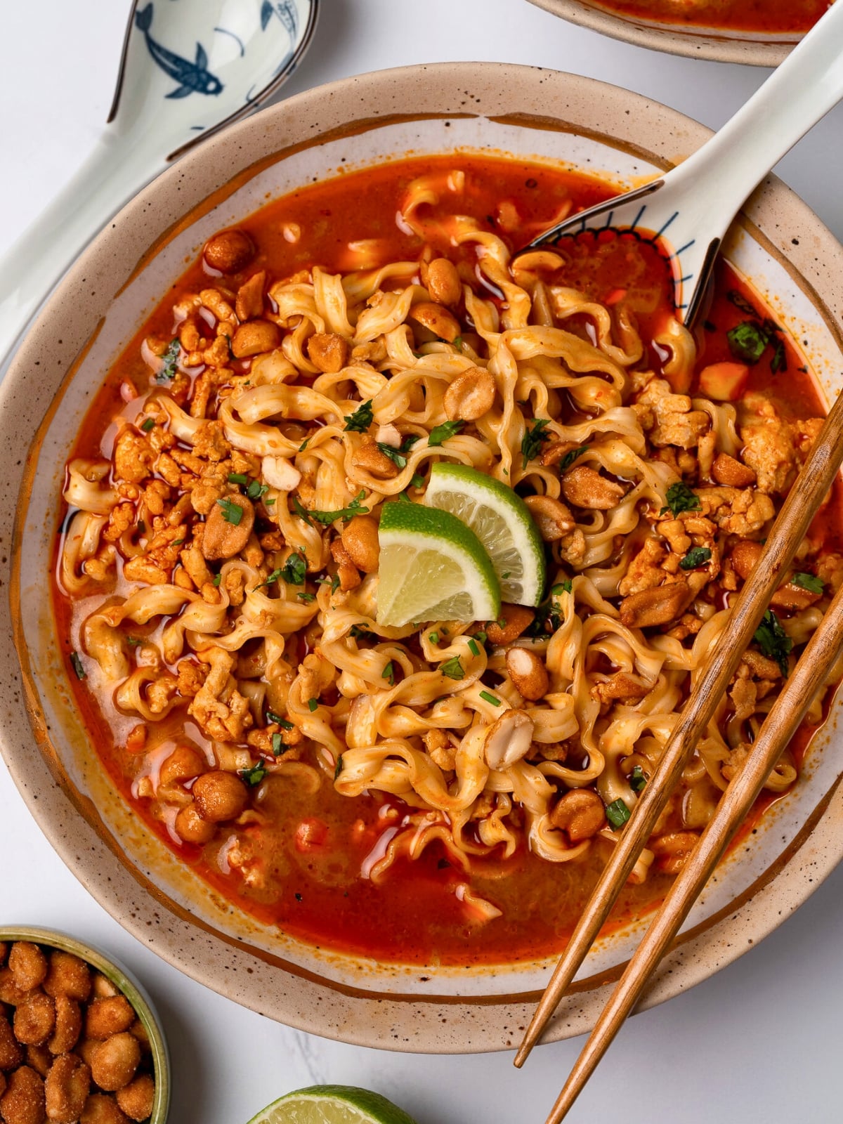 Thai red curry ground turkey and broth in a bowl with Trader Joe's squiggly knife cut noodles, cilantro, and lime wedges