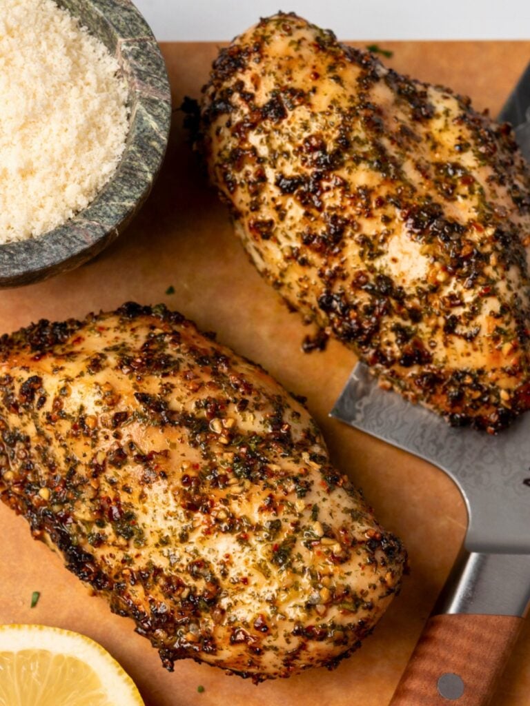 two air fried chicken breasts on a cutting board with grated parmesan and lemon