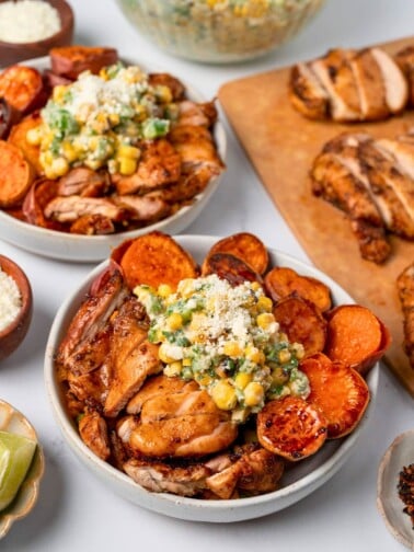 two chicken street corn bowls next to sliced Mexican chicken and garnishes