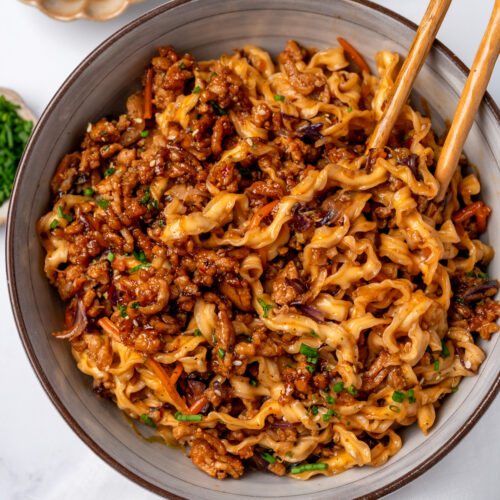 honey garlic ground chicken crumbles in a noodle bowl garnished with chives, sesame seeds, and honey
