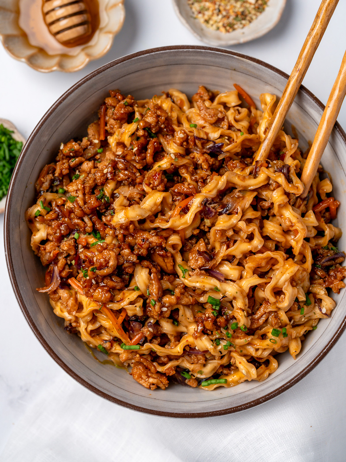 honey garlic ground chicken crumbles in a noodle bowl garnished with chives, sesame seeds, and honey