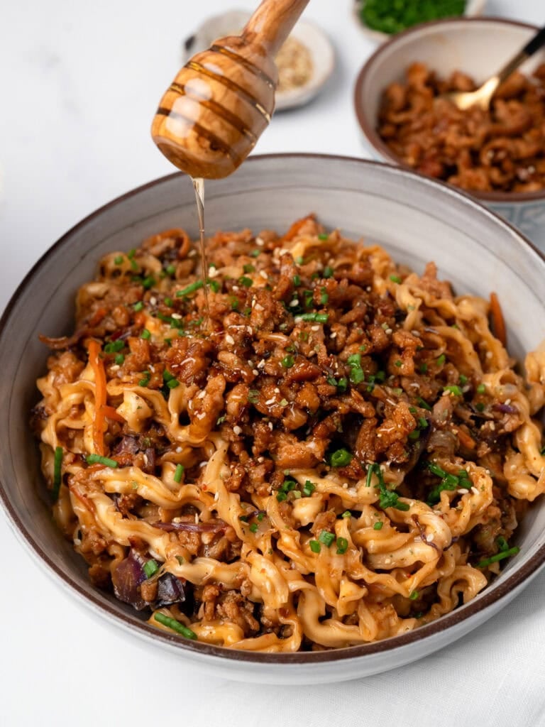 drizzling honey over a bowl of chicken noodles