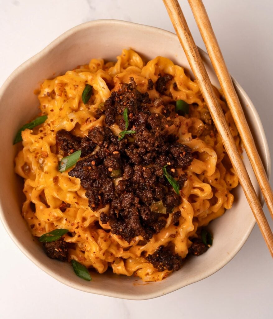 gochujang noodles in a bowl with crisp ground beef, green onions, and chopsticks