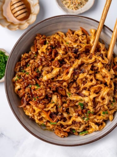 eating honey garlic chicken noodles out of a bowl with chopsticks