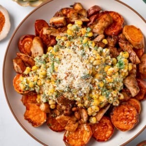 white bowl with roasted sweet potatoes and chopped Mexican chicken topped with street corn salad