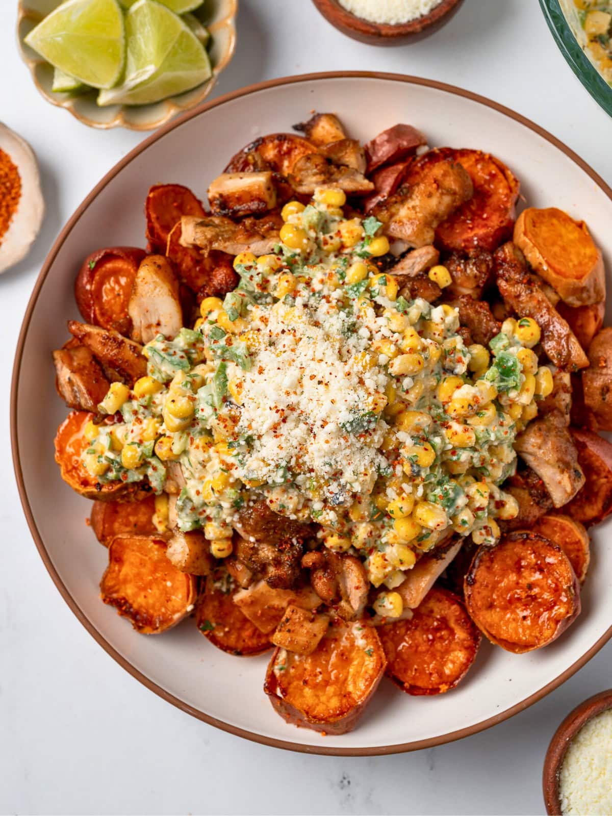 white bowl with roasted sweet potatoes and chopped Mexican chicken topped with street corn salad