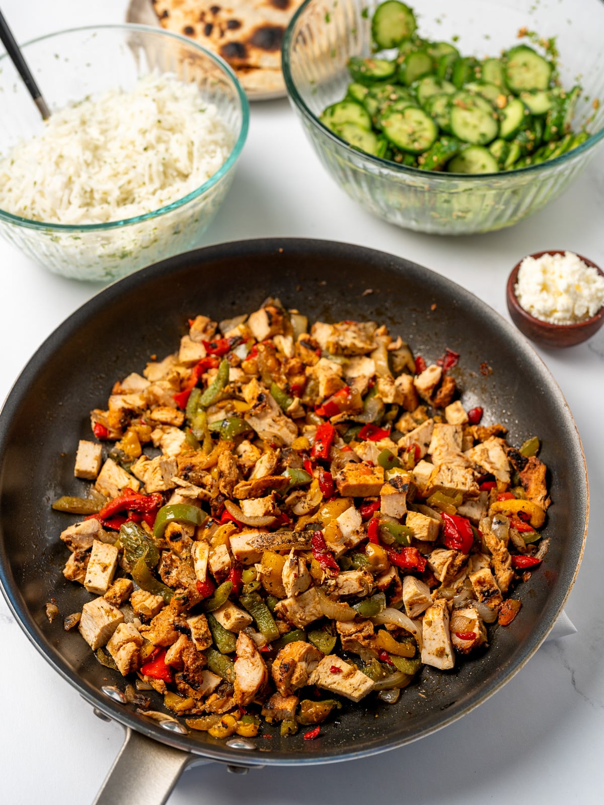 diced grilled chicken breast in a pan with peppers and onions, salsa macha cucumber salad in a glass bowl, and a bowl of cilantro lime basmati rice
