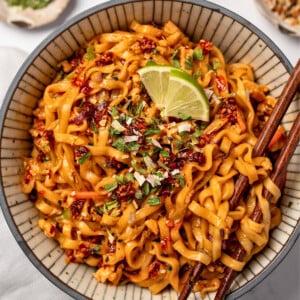 chopsticks in a bowl of noodles that are garnished with lime and dried scallions