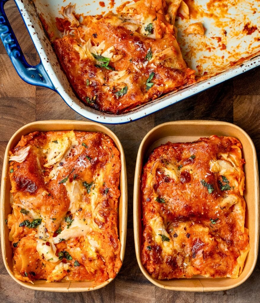 two slices of chicken lasagna in meal prep containers next to the baking dish
