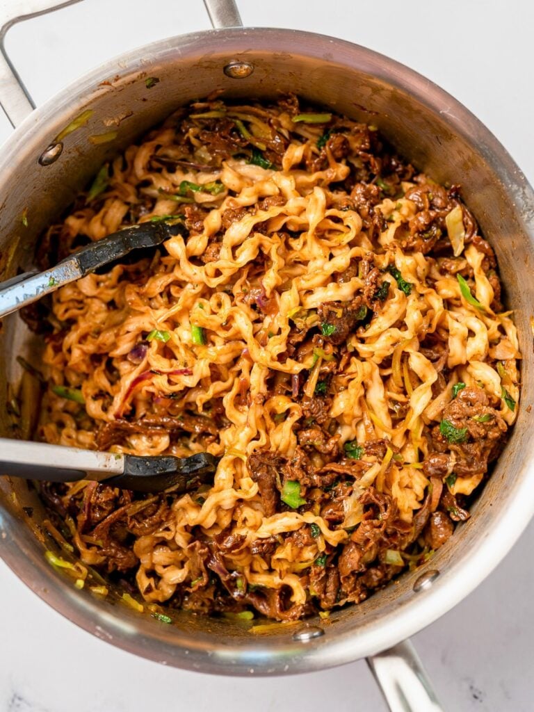 serving beef noodles from a stainless steel pot with tongs