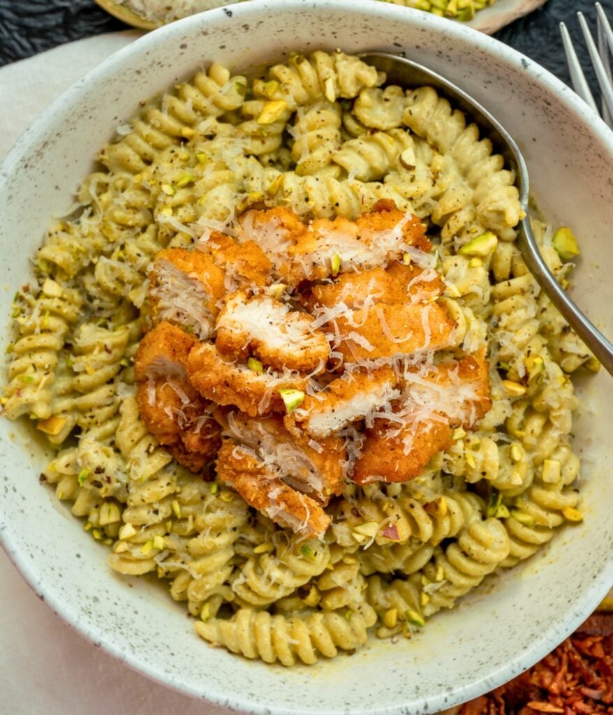 pesto pasta in a bowl topped with parmesan, crispy air fried chopped chicken, and chopped pistachios