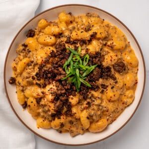 a bowl of gochujang gnocchi topped with sesame garlic ground beef crumbles and sliced green onion