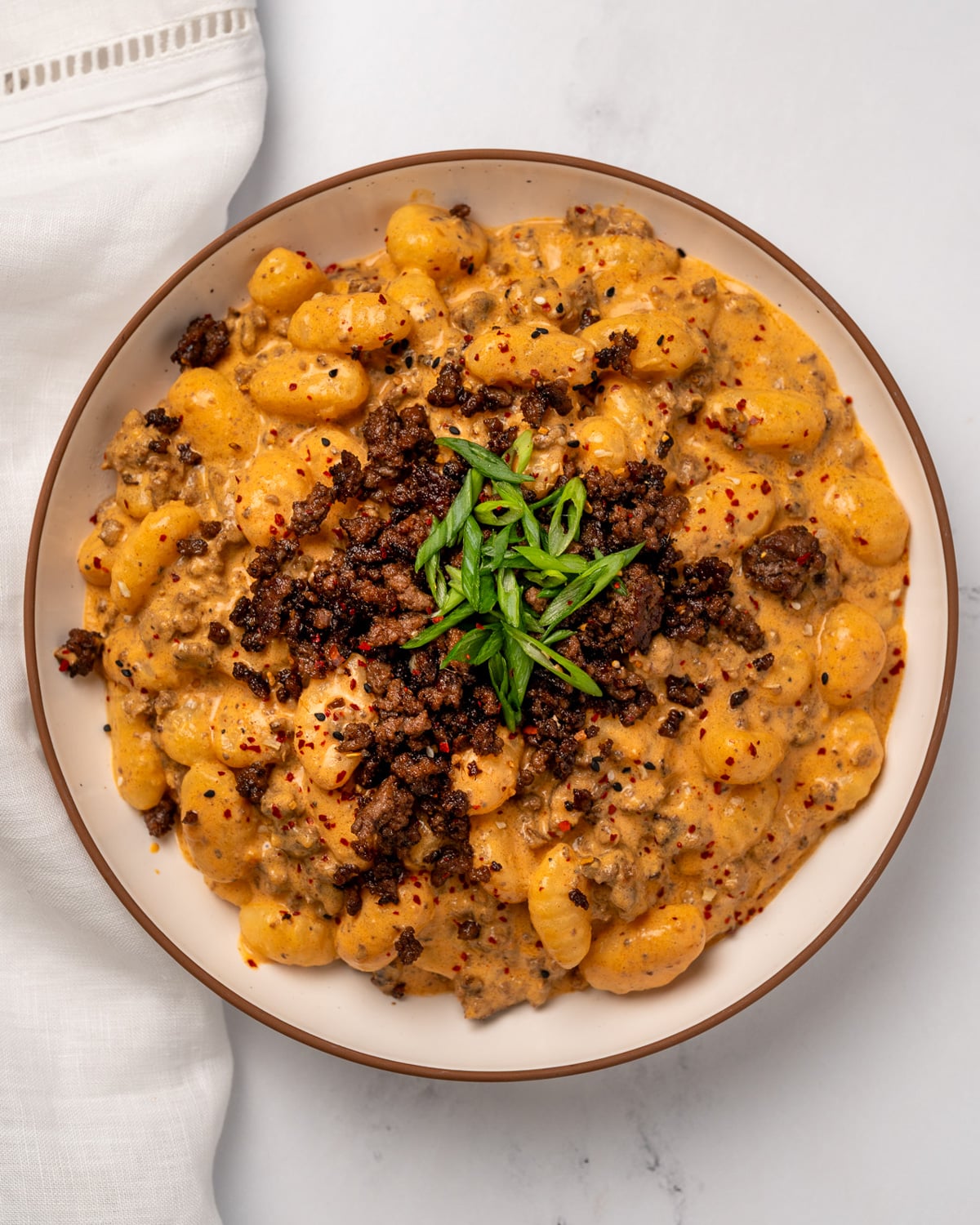 a bowl of gochujang gnocchi topped with sesame garlic ground beef crumbles and sliced green onion