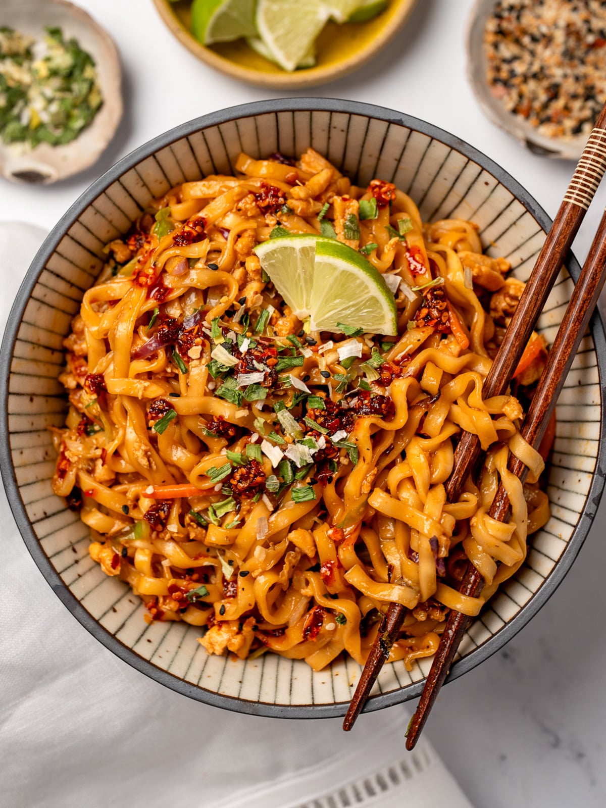 chopsticks in a bowl of firecracker chicken noodles garnished with lime and dried scallions