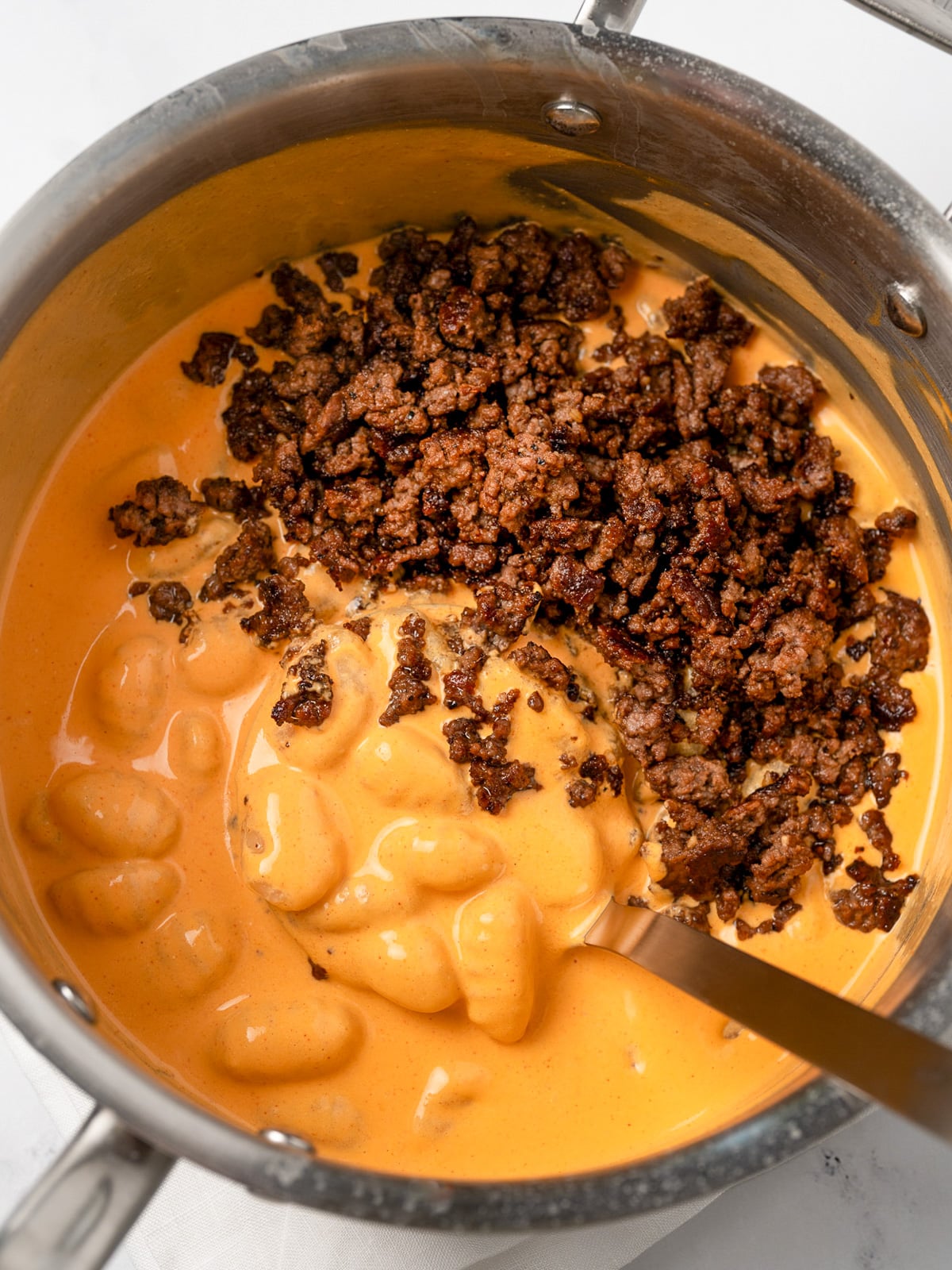creamy gochujang gnocchi in a stainless steel pot with sesame garlic ground beef crumbles on top before mixing together
