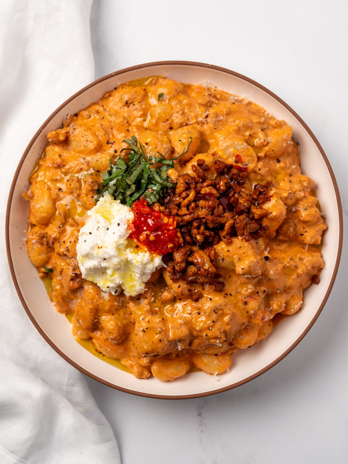 spicy vodka gnocchi in a bowl topped with spicy chicken crumbles, basil, ricotta cheese, and Calabrian chili peppers