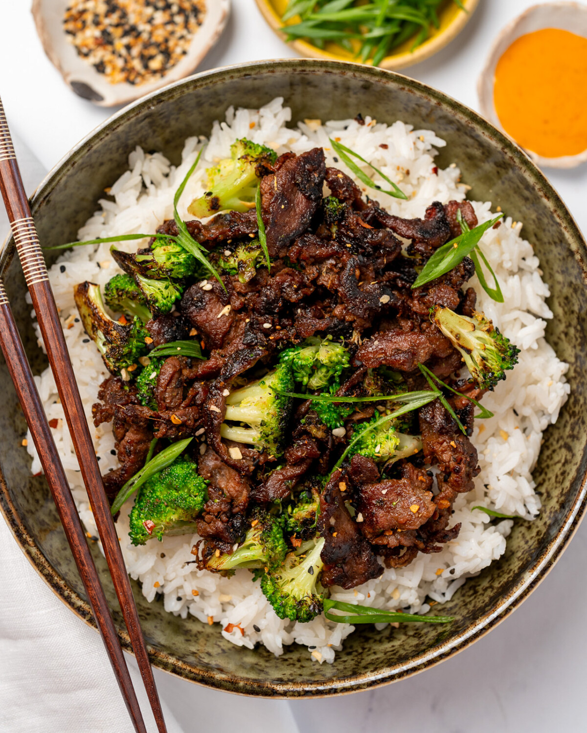 a serving of black pepper beef and broccoli served over steamed jasmine rice in a green bowl