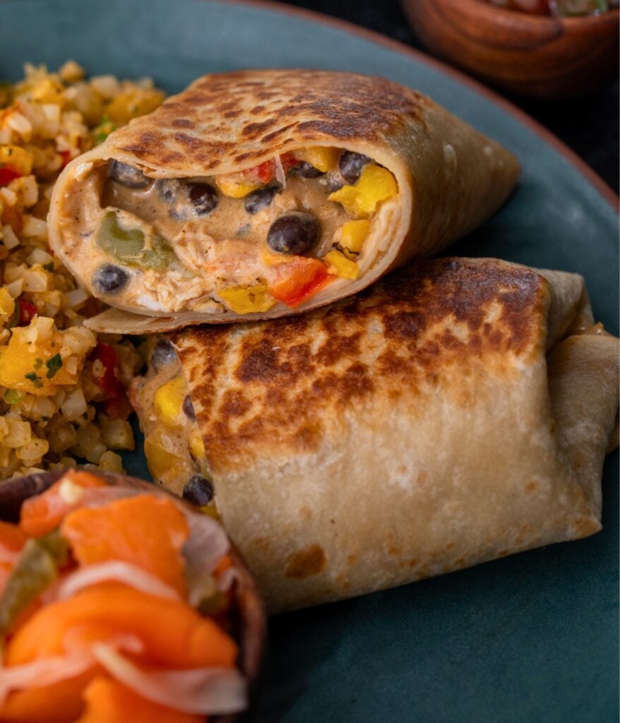 cheesy chicken burrito sliced in half on a plate with Mexican rice and pickled veggies