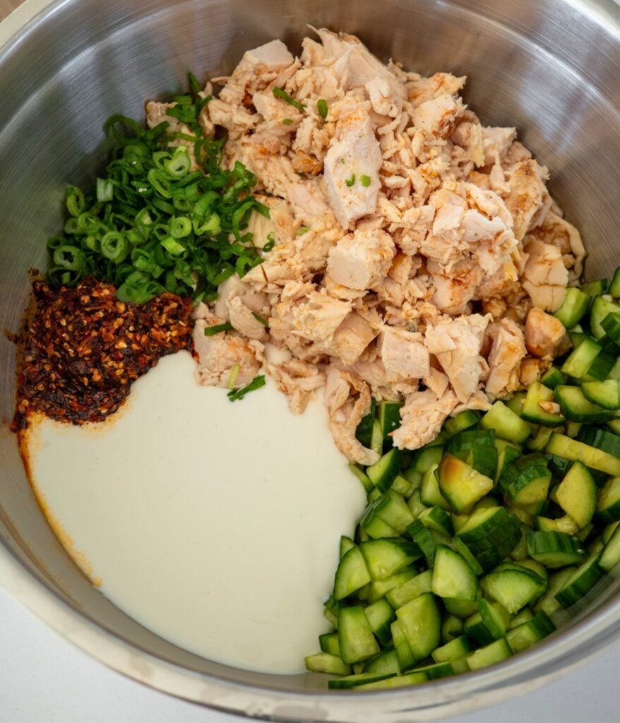 stainless steel mixing bowl with blended cottage cheese, chopped chicken, cucumbers, green onion, and chili crunch