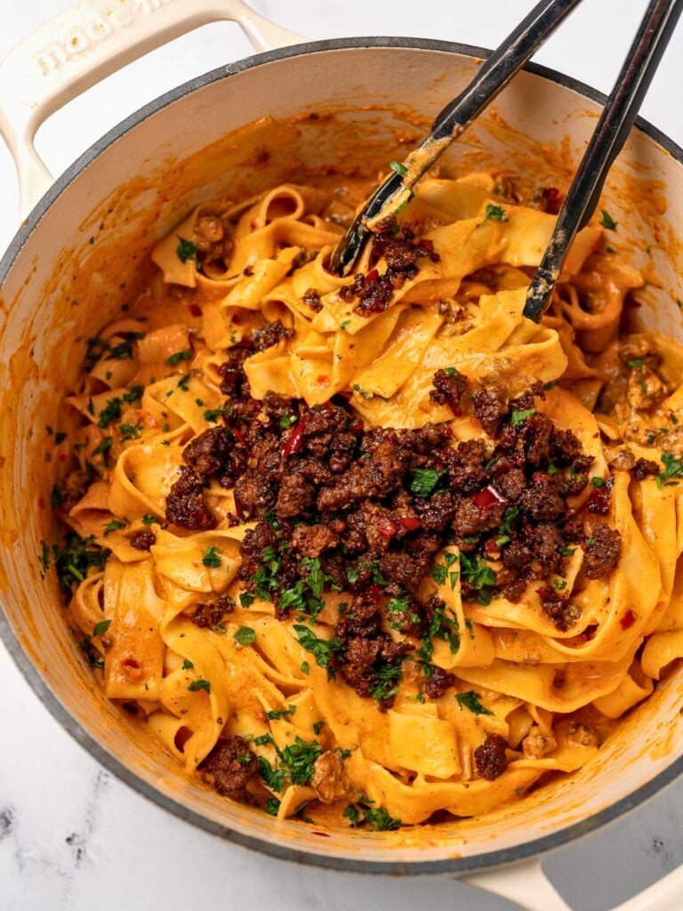 serving red pepper pasta out of a Dutch oven with tongs