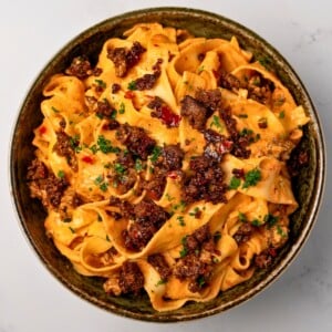 creamy red pepper pasta in a green bowl topped with crispy ground beef and chopped parsley