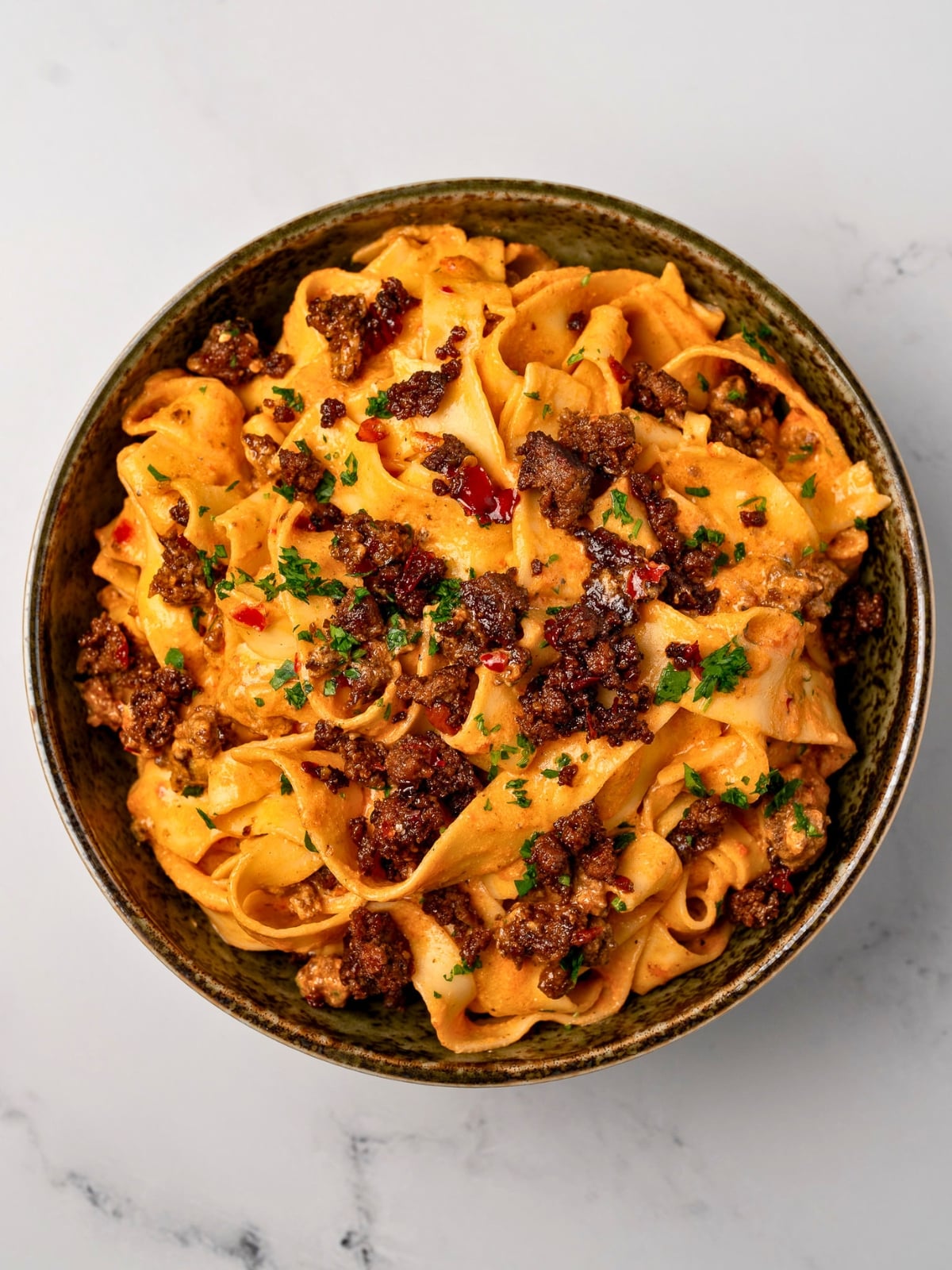 creamy red pepper pasta in a green bowl topped with crispy ground beef and chopped parsley