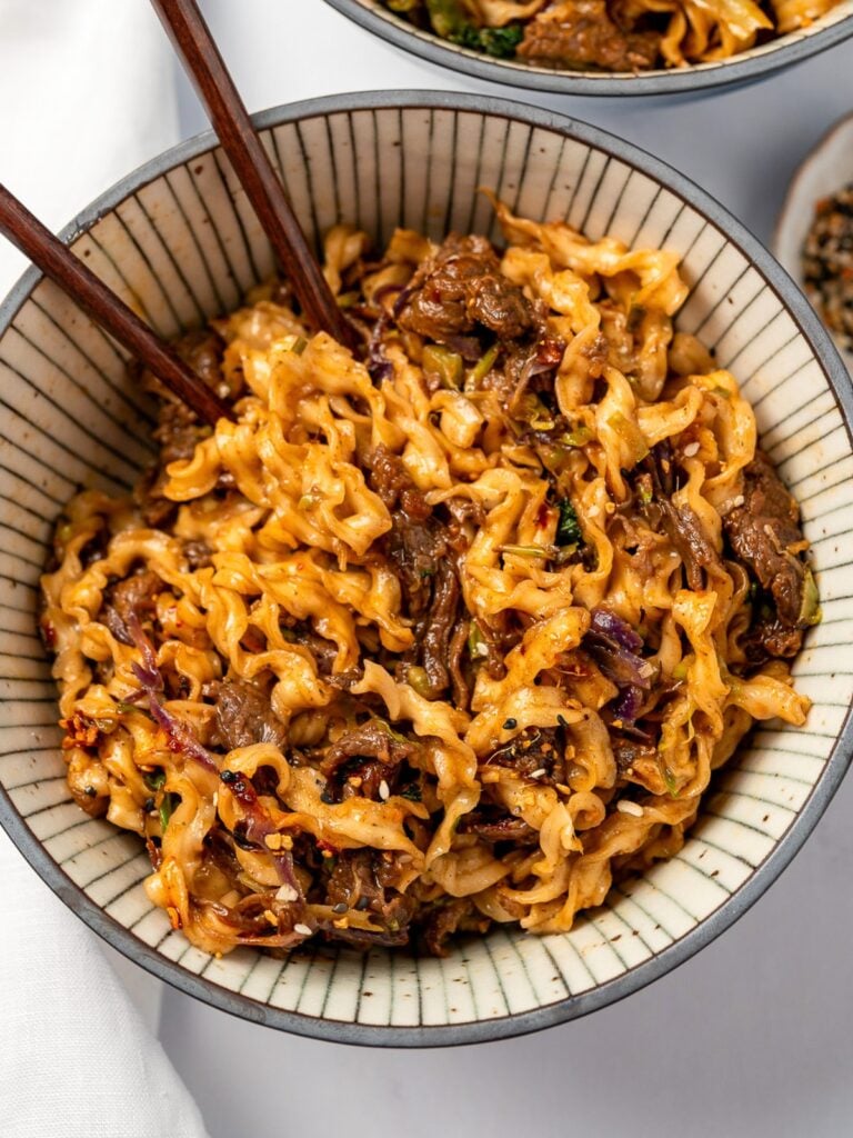 eating stir fried beef noodles from a bowl with brown chopsticks