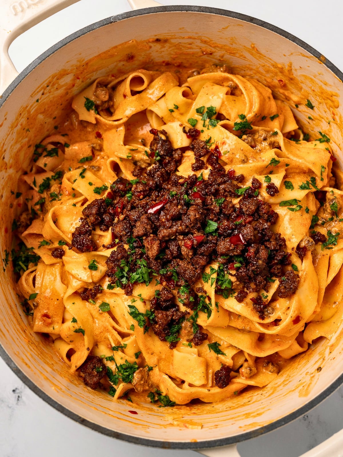 red pepper pasta in a Dutch oven topped with crispy ground beef and fresh parsley