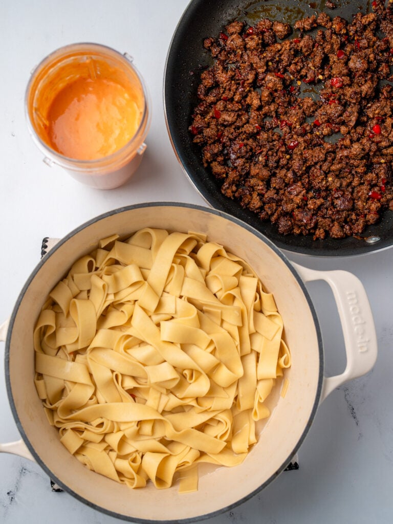 cooked pasta in a Dutch oven, crispy ground beef in a nonstick pan, and blended cottage cheese and red pepper pasta sauce in a blender cup