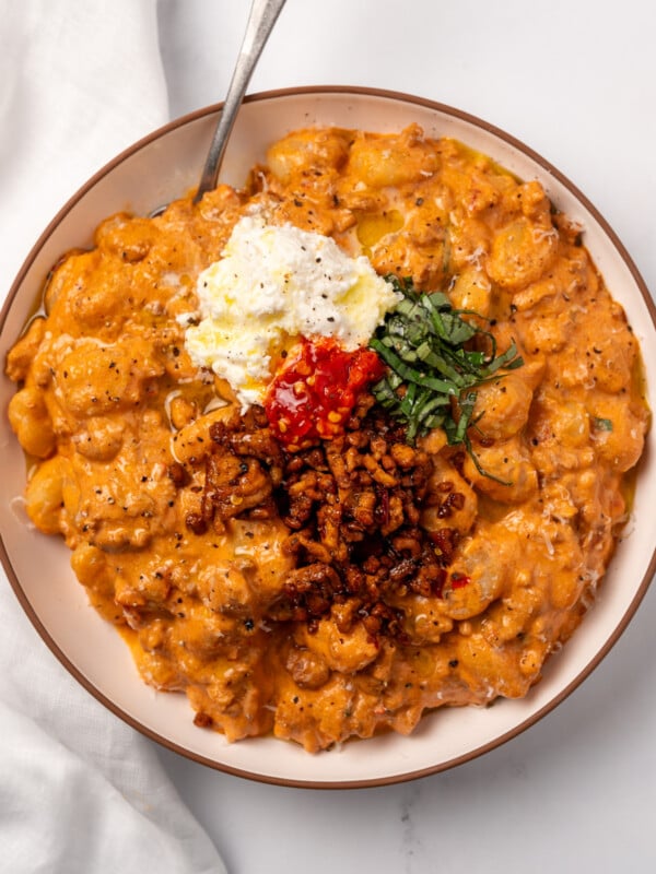 spicy vodka gnocchi in a bowl topped with spicy chicken crumbles, basil, ricotta cheese, and Calabrian chili peppers