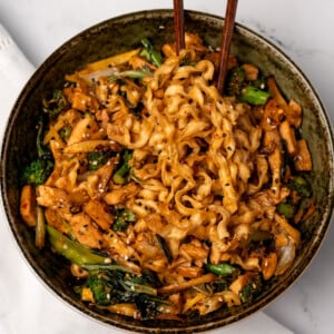 chopsticks in a bowl of chicken stir fry noodles