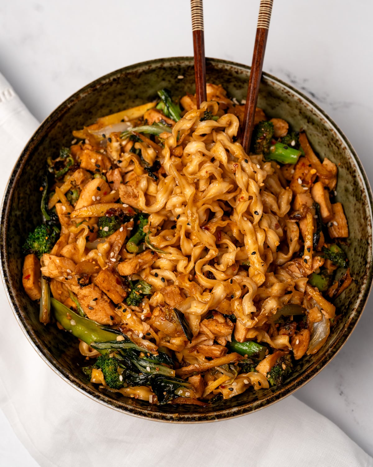 chopsticks in a bowl of chicken stir fry noodles