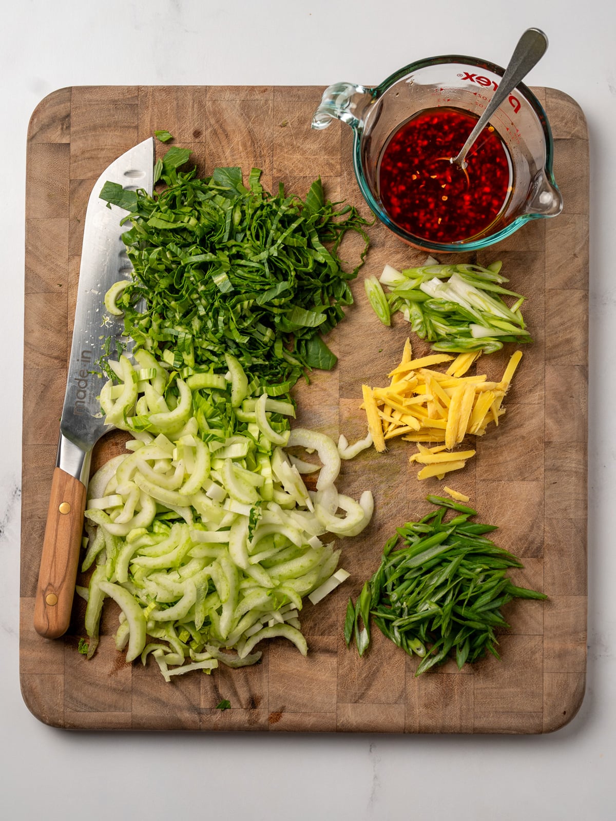 sliced bok choy, ginger matchsticks, sliced green onion, and spicy beef sauce on a cutting board