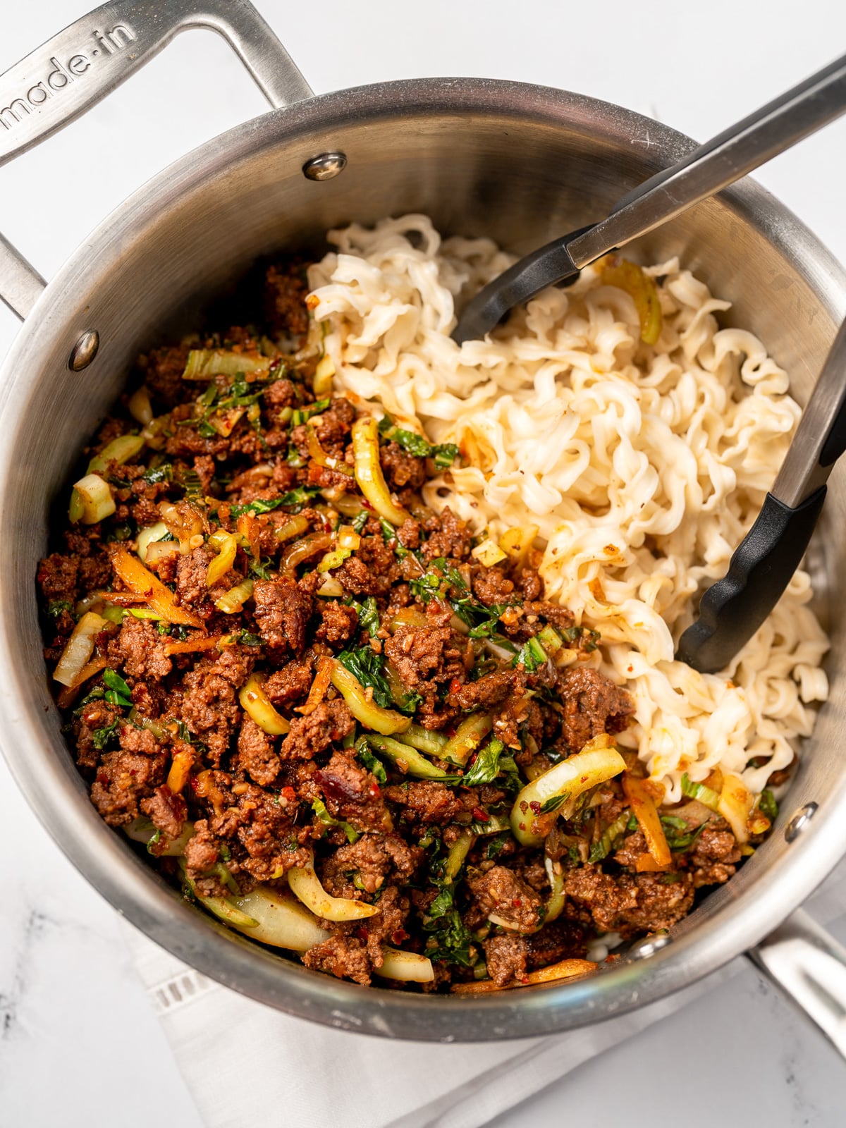mixing cooked instant noodles in a pot with spicy ginger beef stir fry