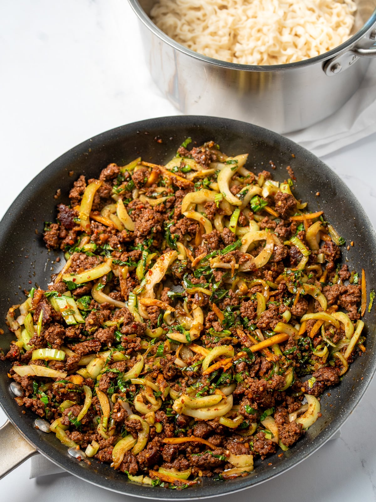 spicy ginger beef stir fry in a pan next to a pot of cooked instant noodles