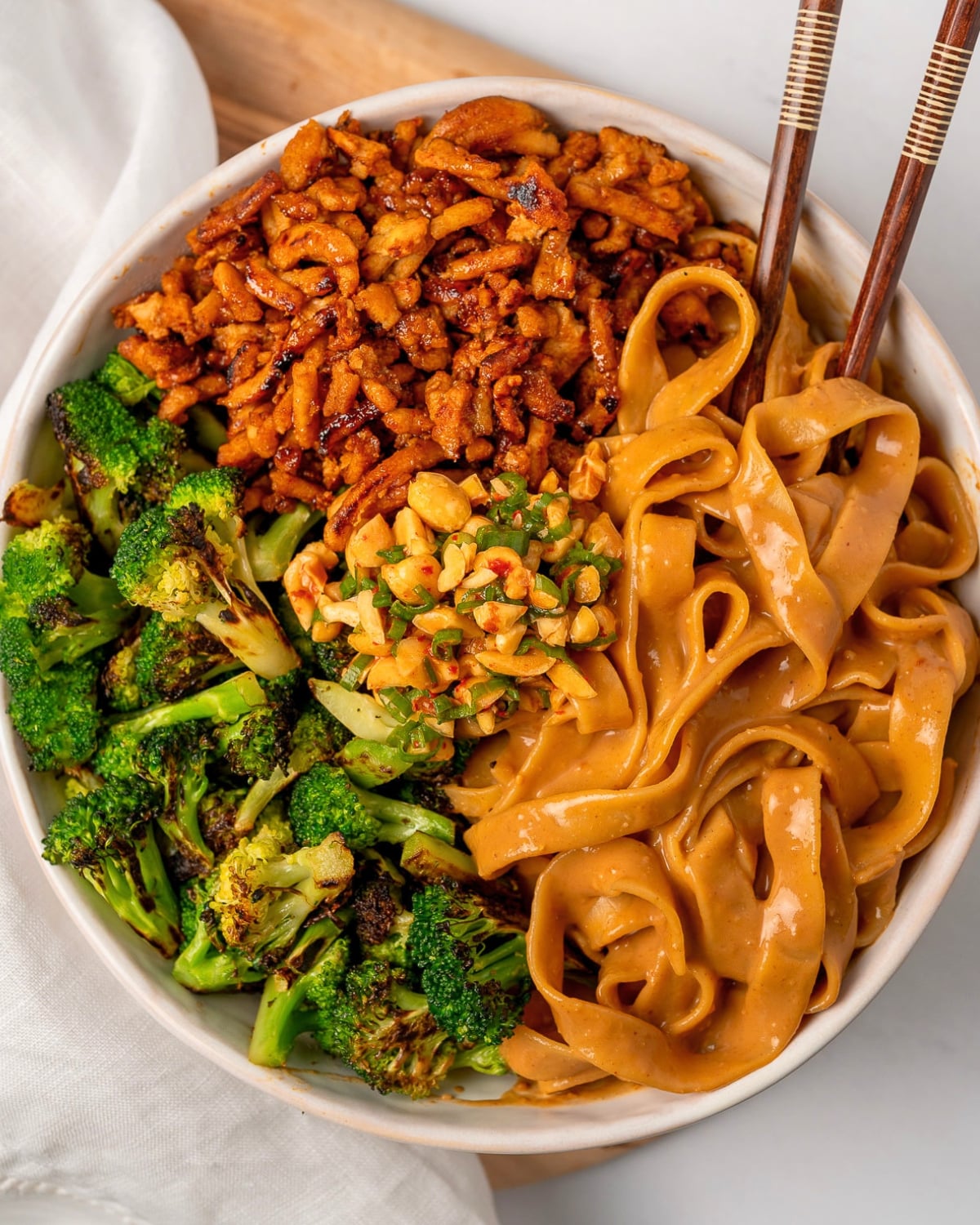 a bowl of ground chicken and broccoli peanut butter noodles with chopsticks