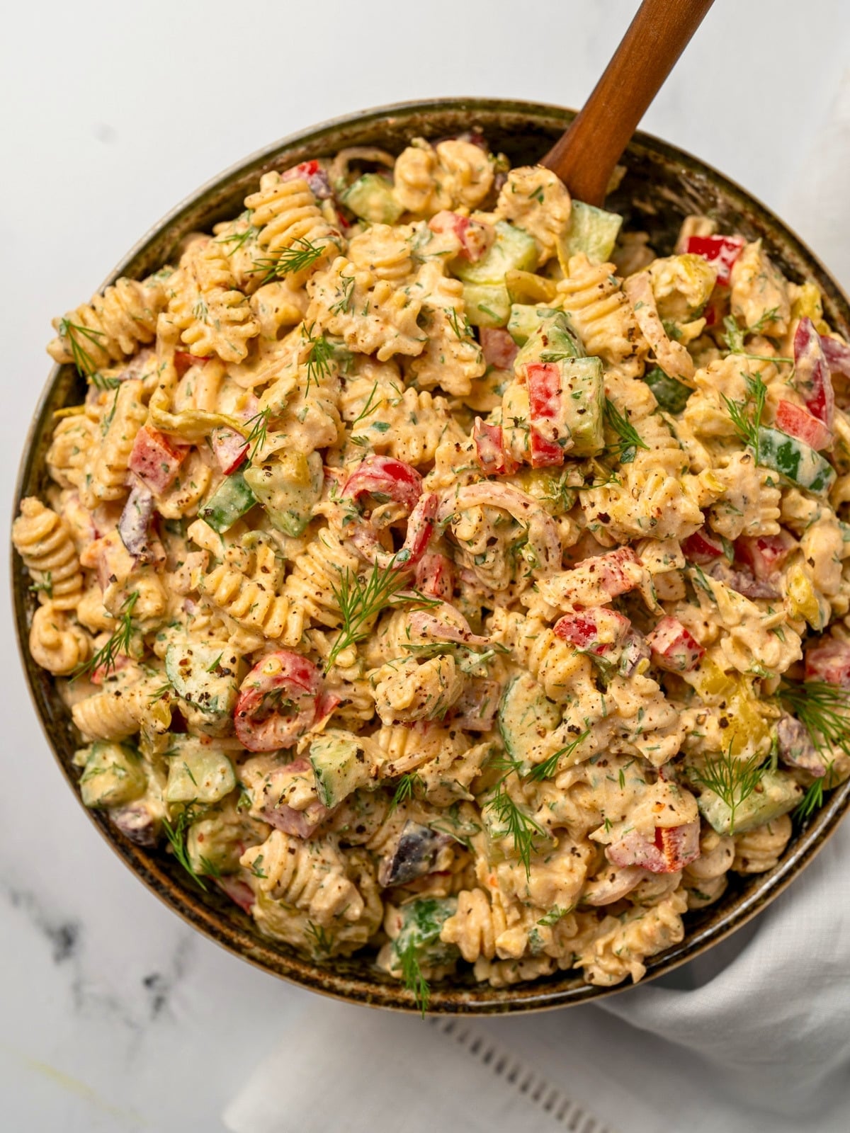 a large bowl of Greek feta pasta salad with a wooden spoon inside