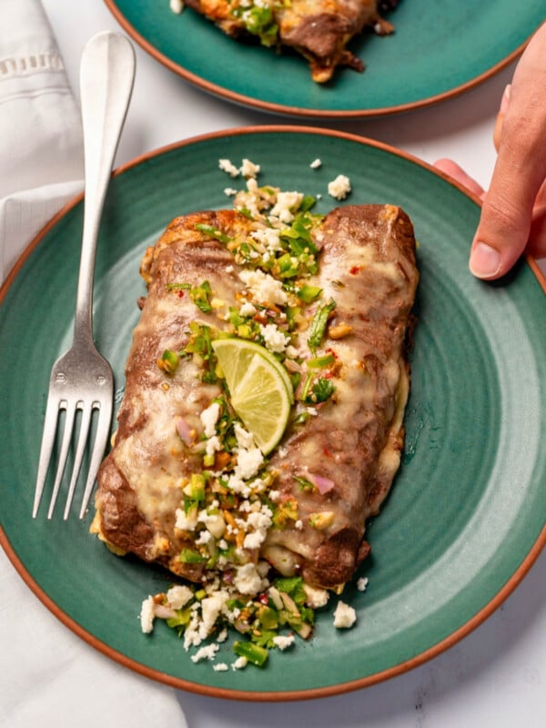 picking up a plate with two enfrijoladas on it garnished with lime wedges, queso fresco, and fresh salsa