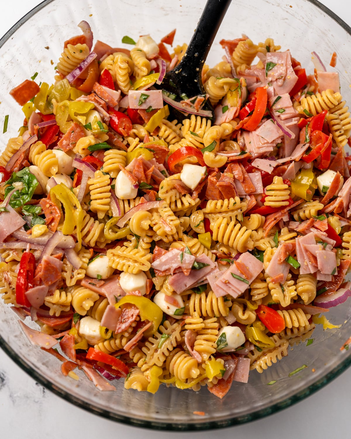 mixing deli pasta salad together with a rubber spatula in a glass mixing bowl
