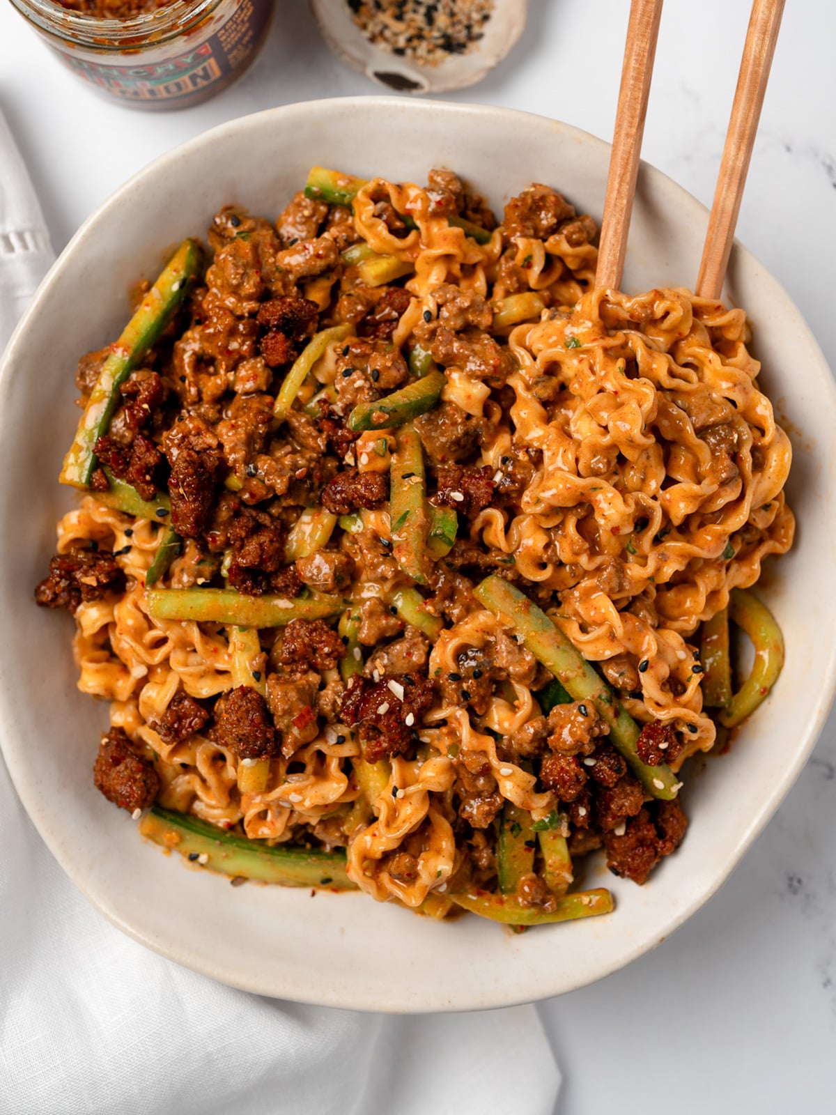 sesame noodles in a bowl mixed with spicy beef and sliced cucumbers