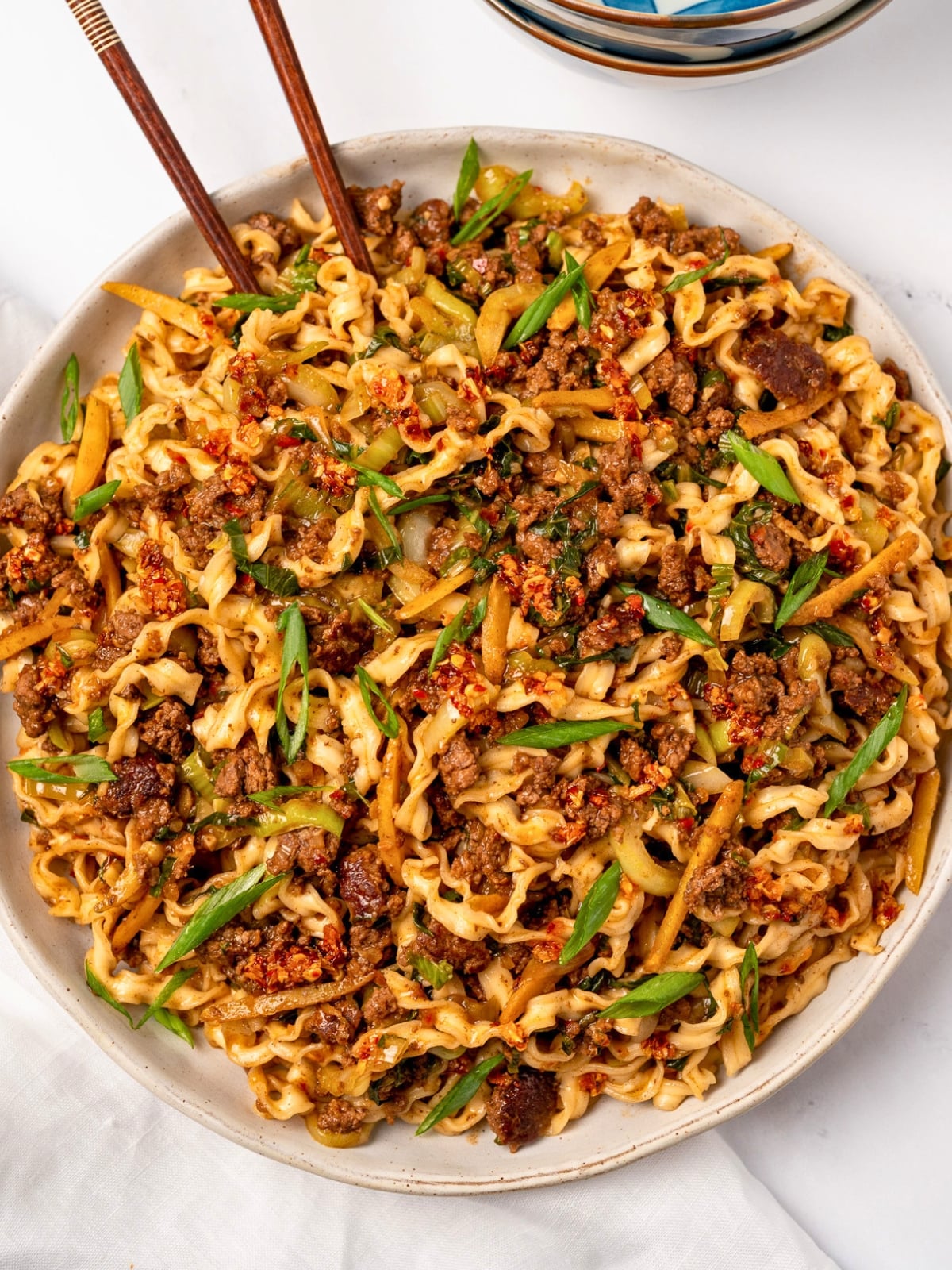 a large bowl of spicy ginger noodles garnished with sliced green onion and crunchy chili onion 